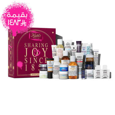 Kiehl’s Advent Calendar gift box in deep red with gold text, displayed next to 24 mini skincare products including Ultra Facial Cream, Calendula Toner, Retinol Serum, and Lip Balm #1. A pink spray-paint graphic on the side calls out the value of the set.