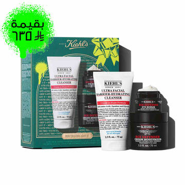 A graphic featuring a dark teal Kiehl’s gift box with white and gold accents on the left. The box contains three products. To the right of the box, the same three products are displayed outside of the box: a white tube of "KIEHL’S ULTRA FACIAL BARRIER-HYDRATING CLEANSER," a small black and red jar of "KIEHL’S AGE DEFENDER EYE REPAIR," and a larger black and red jar of "KIEHL’S AGE DEFENDER CREAM MOISTURIZER." The box is decorated with bright green graphic paint splatters and a bow design and features the text "YOUTH STILL GOT IT" at the bottom.