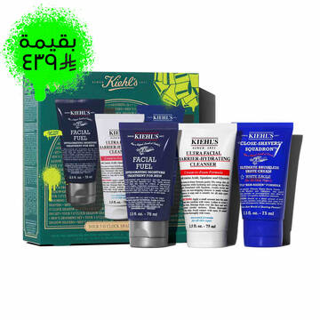 A graphic featuring a dark teal Kiehl’s gift box with gold accents on the left. The box contains three products. To the right of the box, the same three products are displayed outside of the box: a dark blue tube of "KIEHL’S FACIAL FUEL MOISTURIZER," a white tube of "KIEHL’S ULTRA FACIAL BARRIER-HYDRATING CLEANSER," and a dark blue tube of "KIEHL’S CLOSE-SHAVERS SQUADRON ULTIMATE BRUSHLESS SHAVE CREAM." The box is decorated with bright green graphic paint splatters and a bow design, and features the text "YOUR 5 O’CLOCK SHADOW SHAPERS" at the bottom.