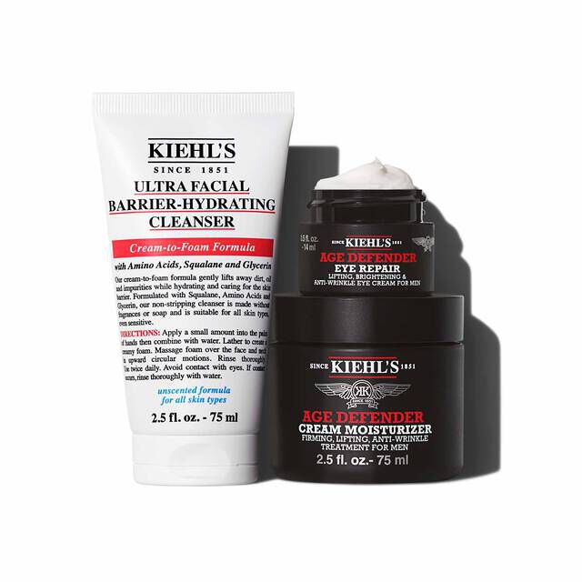 A graphic featuring three Kiehl’s products casting a shadow against a white background: a white tube of "KIEHL’S ULTRA FACIAL BARRIER-HYDRATING CLEANSER," a small black and red jar of "KIEHL’S AGE DEFENDER EYE REPAIR" with visible white cream, and a larger black and red jar of "KIEHL’S AGE DEFENDER CREAM MOISTURIZER". The eye repair and cream moisturizer jars are stacked.