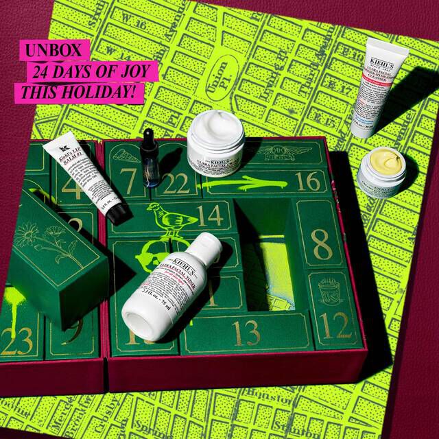 A festive Kiehl’s Advent Calendar box is opened to reveal numbered green drawers with graffiti-style neon yellow and black designsinside. Several skincare products are displayed in front, including the Calendula Herbal-Extract Toner, Creamy Eye Treatment with Avocado,and Midnight Recovery Omega-Rich Cloud Cream. A bright pink banner at the top left reads: “UNBOX 24 DAYS OF JOY THIS HOLIDAY!”