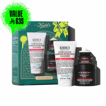 A graphic featuring a dark teal Kiehl’s gift box with white and gold accents on the left. The box contains three products. To the right of the box, the same three products are displayed outside of the box: a white tube of "KIEHL’S ULTRA FACIAL BARRIER-HYDRATING CLEANSER," a small black and red jar of "KIEHL’S AGE DEFENDER EYE REPAIR," and a larger black and red jar of "KIEHL’S AGE DEFENDER CREAM MOISTURIZER." The box is decorated with bright green graphic paint splatters and a bow design and features the text "YOUTH STILL GOT IT" at the bottom.
